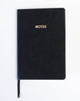 A black colored vegan leather notebook with gold foil text reading "NOTES" across the front photographed against a white background.