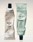 Squeezed tubes of the gray sandal and green bergamot hand lotions placed next to each other