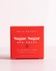 Red cube box packaging that has white text on the front that reads "NCLA Beauty Sugar, Sugar Red Roses. All Natural Lip Scrub". Cover has a small red rose illustrated under the name