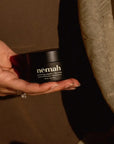 Renewing Nipple + Lip Balm in hand on neutral background.
