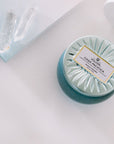 Voluspa Casa Pacific Baby Blue Candle next to book corner with two crystals.