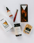 Compartes The Nightcap Chocolate Bar, Corkcicle Whiskey Wedge Glass, Mielle Citrus Peeler, Art of Caramel Kentucky Bourbon Black Pepper Popcorn, Jack Rudy Cocktail Co. Aromatic Bitters and Jack Rudy Cocktail Co. Bourbon Cocktail Cherries laid out on white background