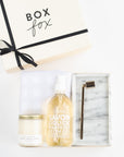 BOXFOX Original creme Housewarming Gift Box packed with Geometry Linen Plaid Tea Towel, Mielle Marble Tray, Vivie Gold Candle Snuffer, Beverly + 3rd Home Sweet Home Candle, and Compagnie de Provence 16.7 oz Liquid Hand Soap.