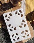 white breeze block ice pack on piece of wood in a picnic setting. Ice pack has cut outs resembling mosaic pattern