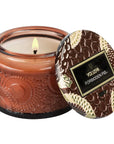 Amber colored petite glass jar candle - forbidden fig scent. Candle burning on white background.
