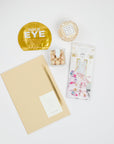 BOXFOX Gold Bullet Pen, Compartes Cake & Sprinkles White Chocolate Bar, Sugarfina Birthday Cake Cookie Bites, Voluspa Bergamot Macaron Candle and Vitamasque Gold Eye Mask. on white background