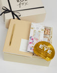 BOXFOX Creme Gift box containing Notem Gold Stripe notebook, BOXFOX Gold Bullet Pen, Compartes Cake & Sprinkles White Chocolate Bar, Sugarfina Birthday Cake Cookie Bites, Voluspa Bergamot Macaron Candle and Vitamasque Gold Eye Mask.