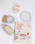 Table for Two ready to ship products including "Table for Two" cookbook, Le Creuset spoon rest, Branche olive oil, The Salt, and marble salt cellar