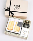 BOXFOX Original creme Pop Fizz Clink Gift Box packed with Voluspa Crisp Champagne Candle, Vinoos Champagne Gummies, Viski Gold Champagne Stopper, and Viski Pair of Champagne Flutes.