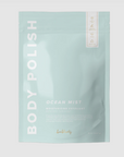 Rectangular, sealed, light blue plastic bag with white text that reads "BODY POLISH" on the side and "OCEAN MIST MOISTURIZING EXFOLIANT" in bottom right. Photographed on grey background.