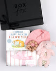 BOXFOX black gift box next to open box containing a book, swaddle, teether, baby beanie and bunny rattle.