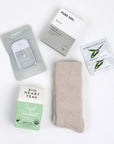 BOXFOX Creme Gift Box items including Royal Treatmint Big Heart Tea, Pure Sol Charcoal Eye Pads, BOXFOX tan cozy socks, set of Herban Essentials Eucalyptus wipes and Touchland hand sanitizer laid out on white background