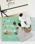 BOXFOX Original creme New Family Gift Box packed with PEHR cozy grey striped onesie 3-6 months, Jellycat puppy lovey, Our Animal Neighbors book, Pipette baby oil, Alva sage green teether, and Alva sage green beanie