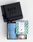 Black BOXFOX gift box next to open box including collapsible cup, tin candle and two art of tea sachets