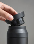 Hand holding lid to black travel tumbler.