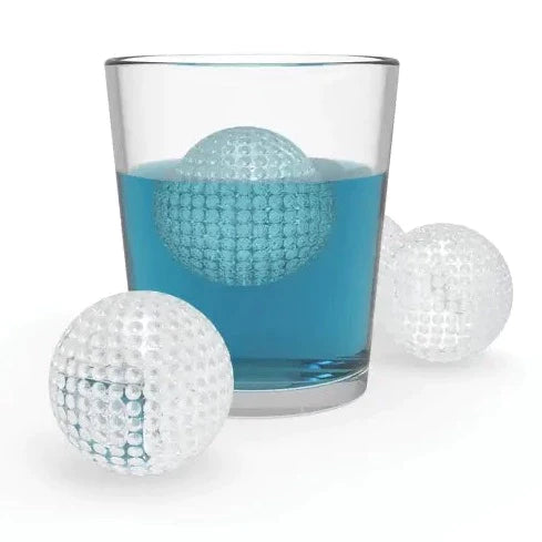 3 golf ball ice cubes. one in a cup with blue liquid. the other 2 are outside the cup next to the cup