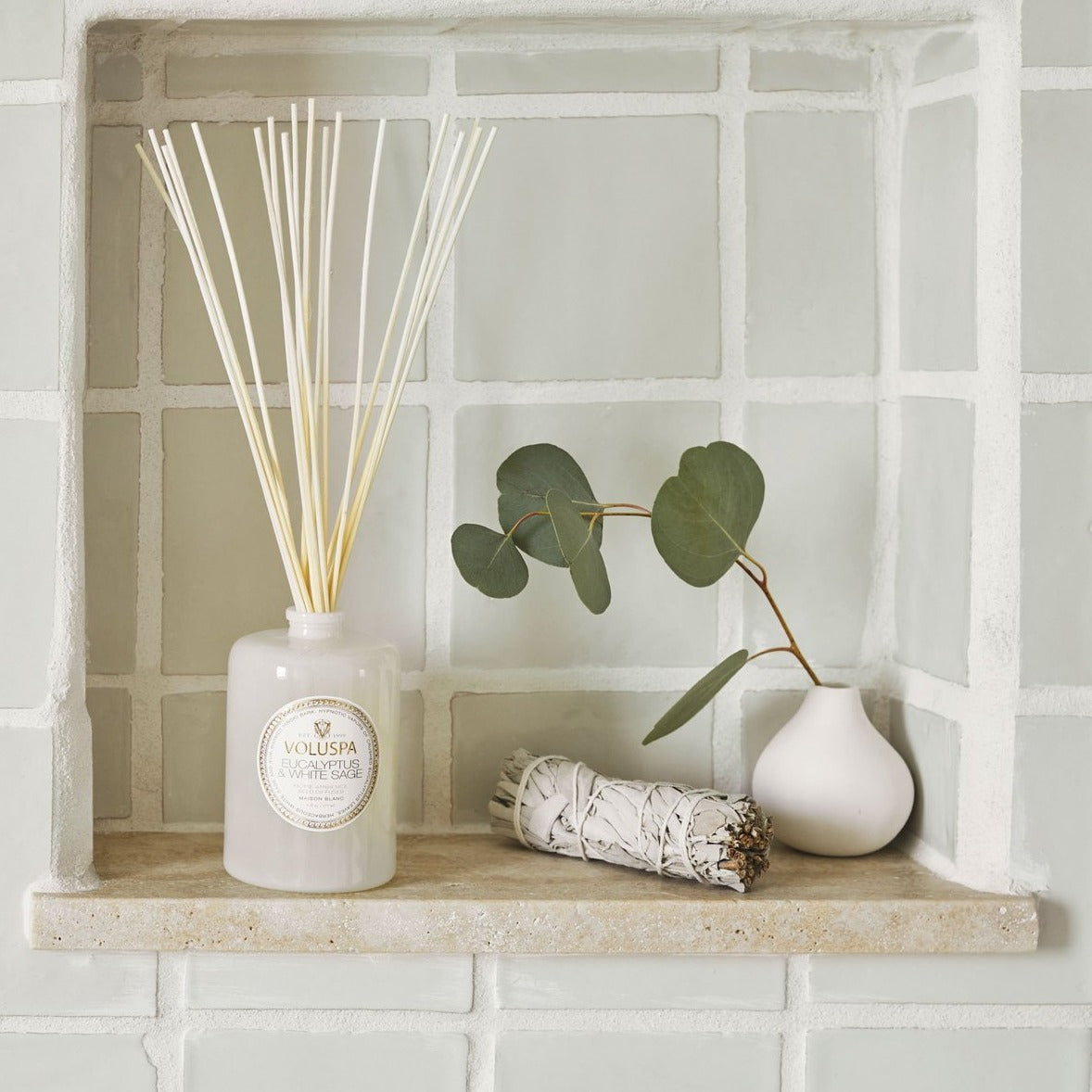 Diffuser in shower alcove with sage smudge stick and eucalyptus branch in bud vase.