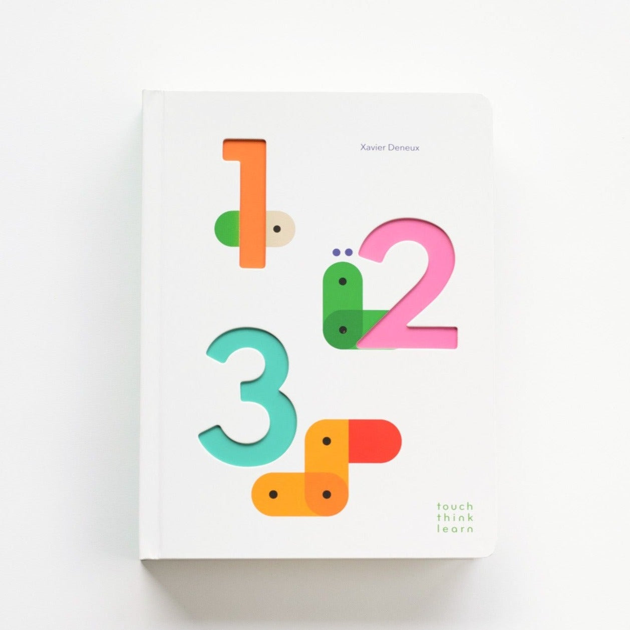 A white board book with cutouts in the shapes of numbers 1, 2 and 3 with colored paper on first page showing through. Text on book reads, &quot;Xavier Deneux touch think learn&quot;. Photographed on white background.