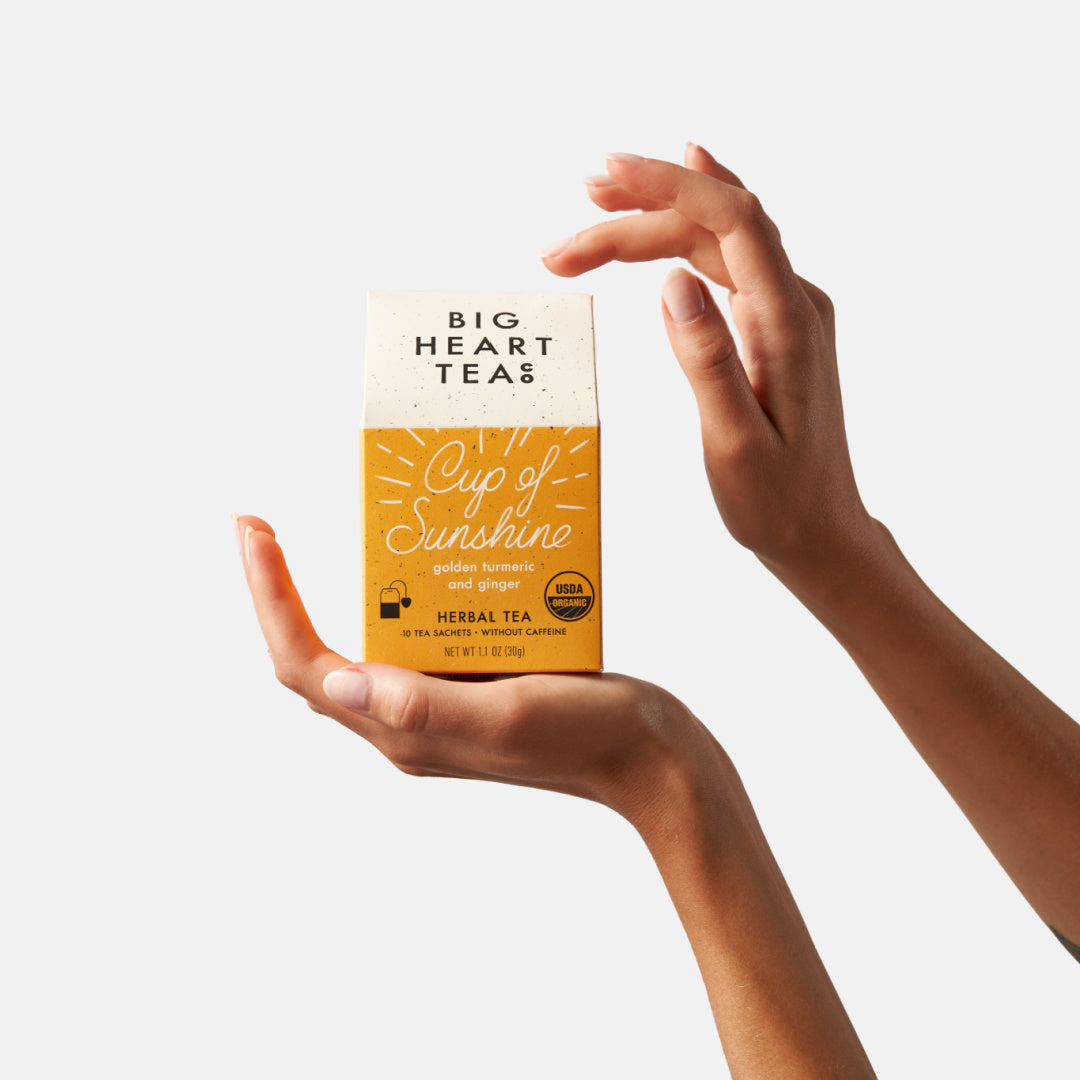 Yellow tea box packaging held by two hands on a white background.