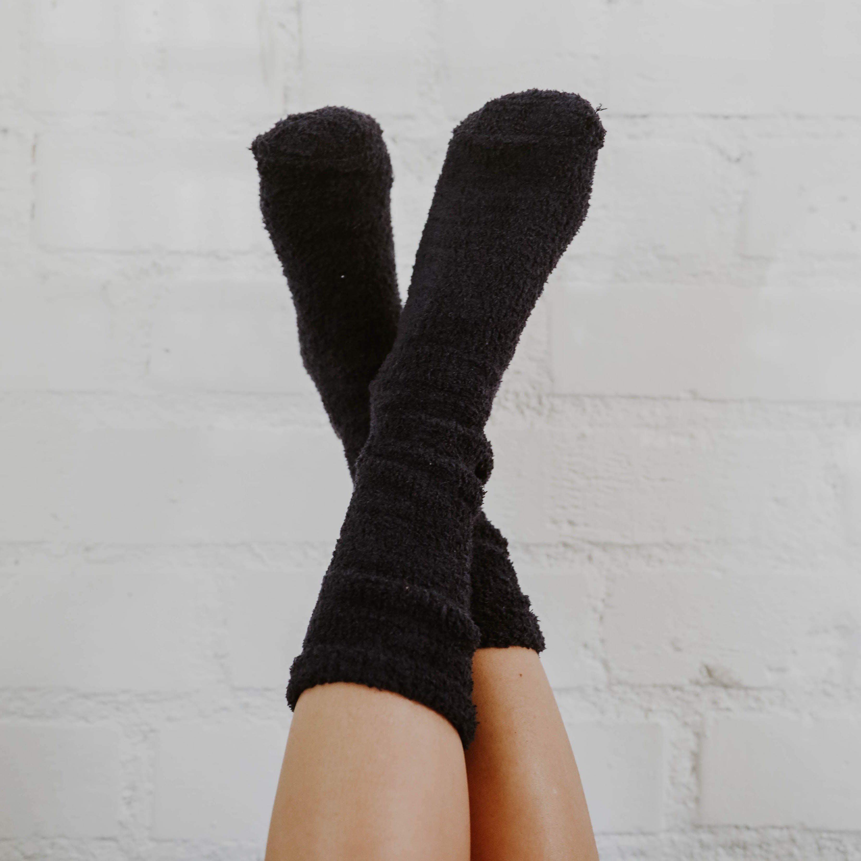 A girl with tan legs wearing mid-calf navy blue fuzzy socks with her legs up in the air criss-crossing against a white background