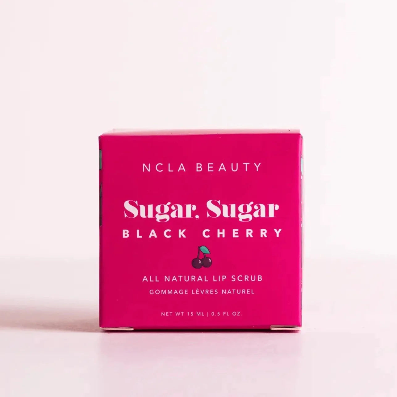 Magenta square box with white text on the front. Text reads "NCLA Beauty Sugar, Sugar Black Cherry All Natural Lip Scrub". Has a small cherry illustration under the name