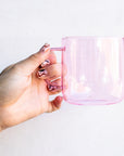 Hand holding empty pink glass mug.