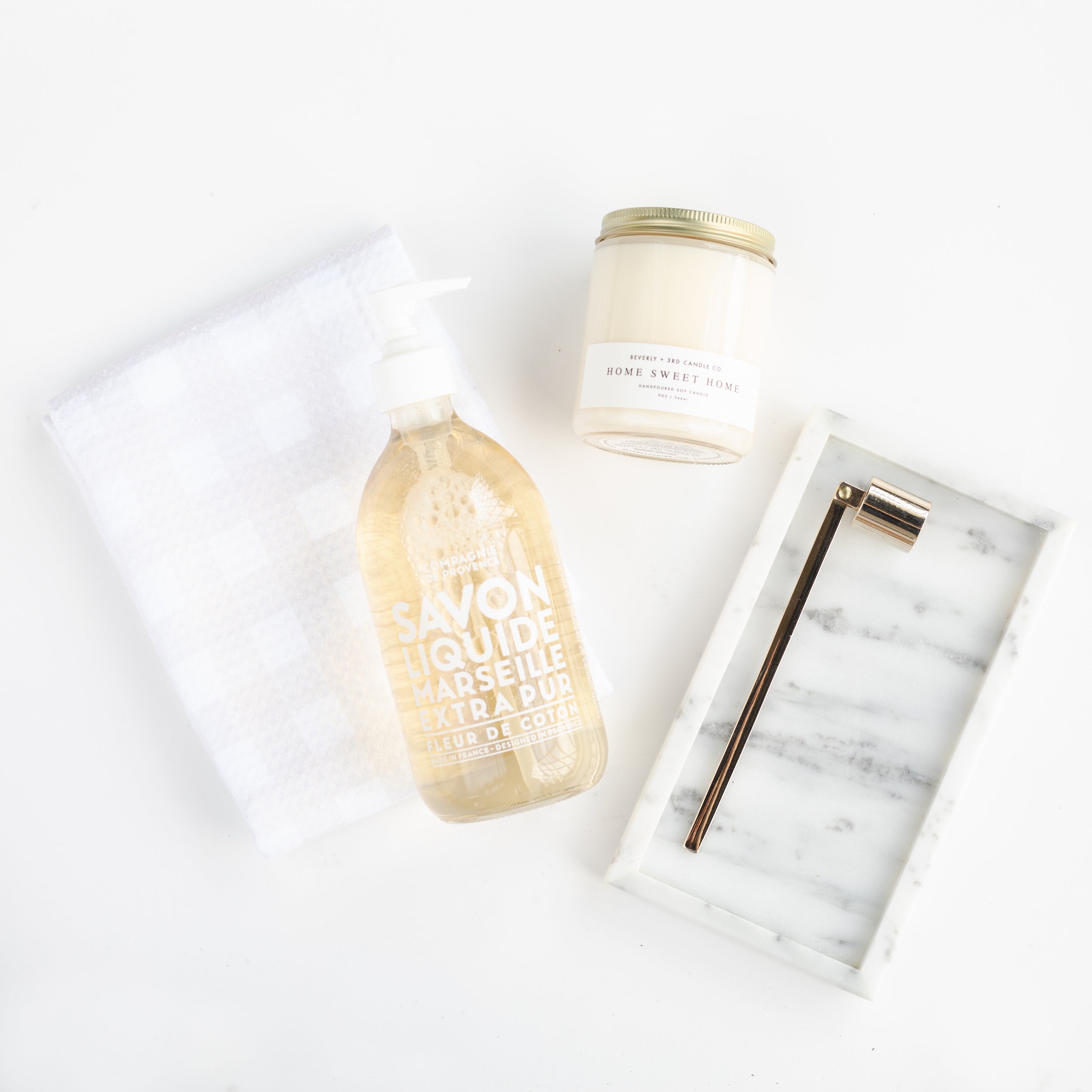 Geometry Linen Plaid Tea Towel, Mielle Marble Tray, Vivie Gold Candle Snuffer, Beverly + 3rd Home Sweet Home Candle, and Compagnie de Provence 16.7 oz Liquid Hand Soap laid out on white background.