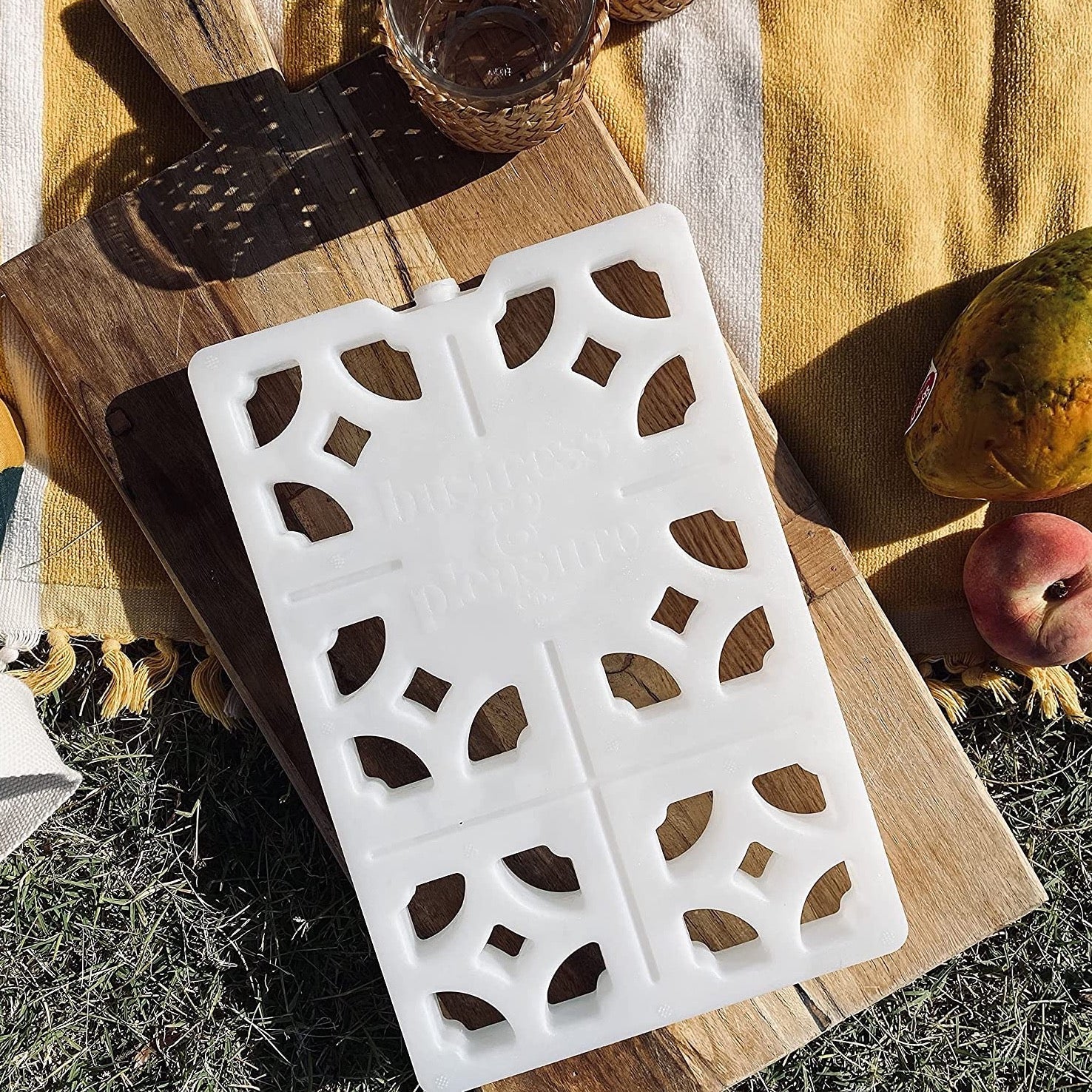 white breeze block ice pack on piece of wood in a picnic setting. Ice pack has cut outs resembling mosaic pattern