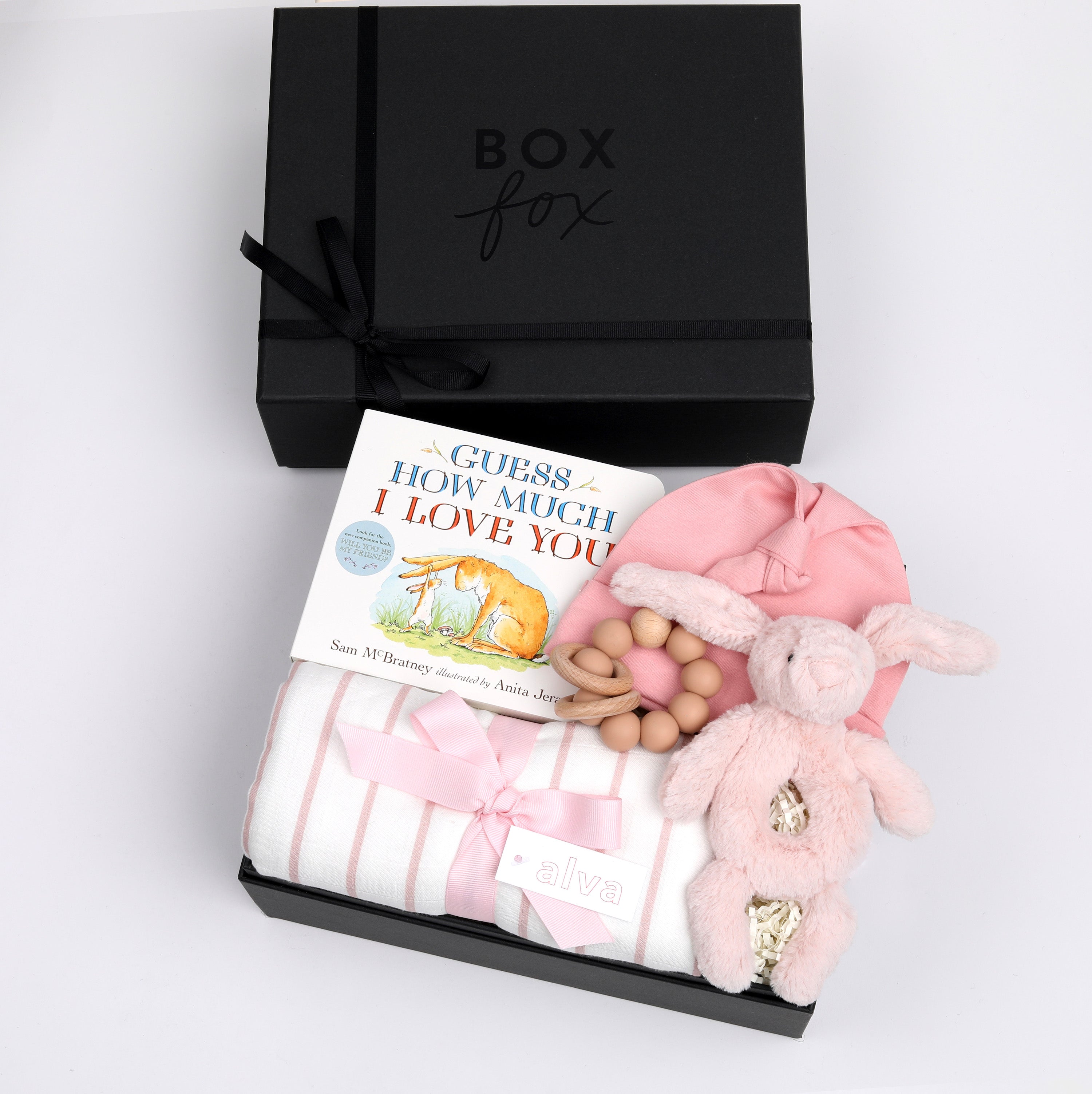 BOXFOX black gift box next to open box containing a book, swaddle, teether, baby beanie and bunny rattle.