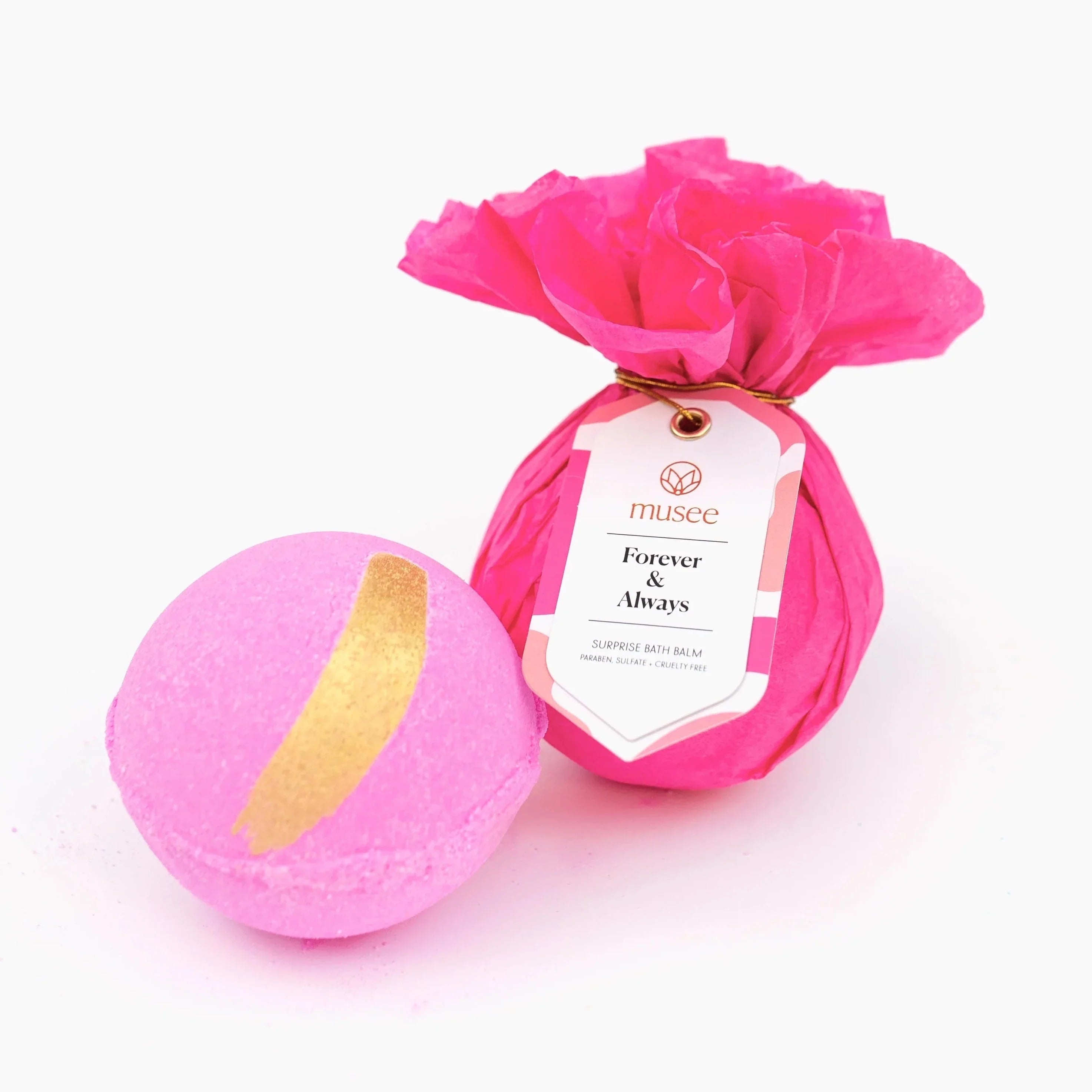 Hot pink tissue paper for bath bomb with a pin and white tag with black text that reads "forever & always". Actual bath bomb is pink with a gold accent stripe at the top