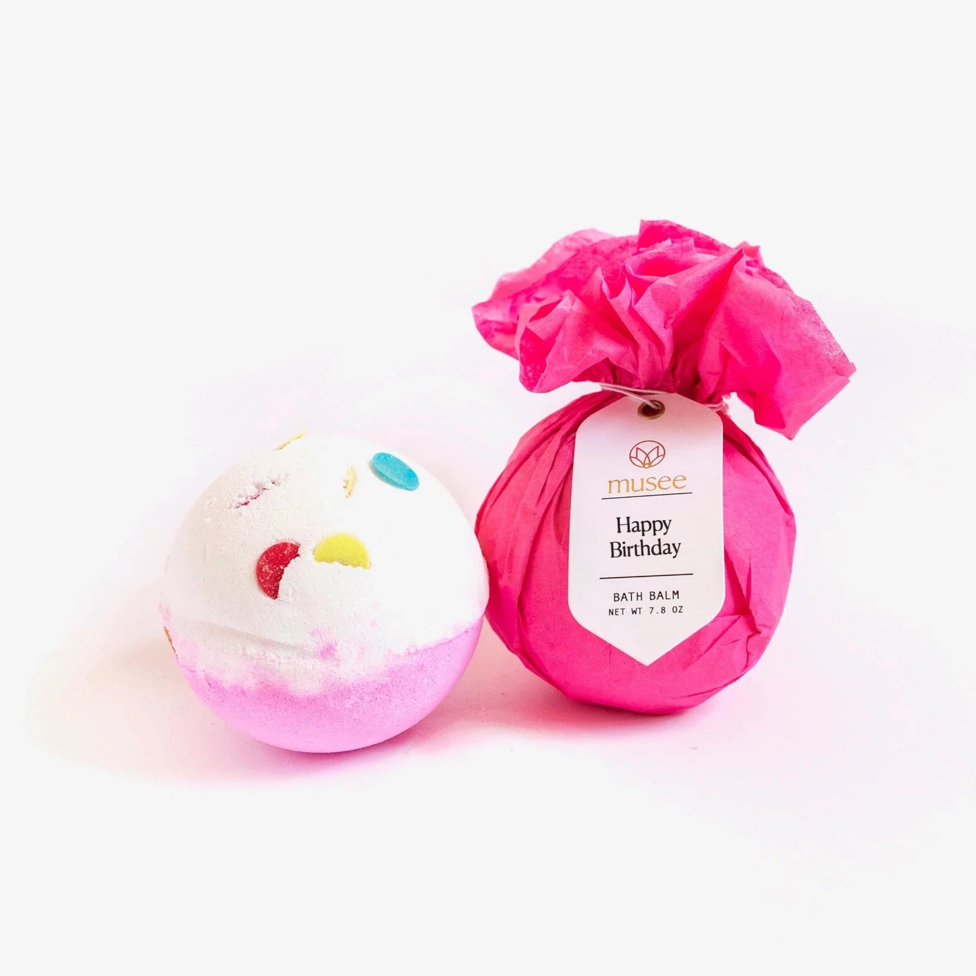 happy birthday bath bomb where the top half is white with confetti and the bottom half is pink. next to it is a wrapped bath bomb in pink tissue paper