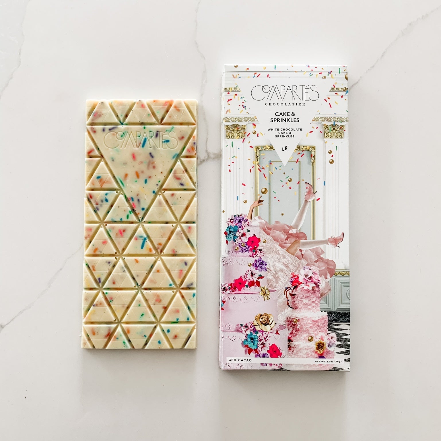 White chocolate bar with sprinkles next to packaging featuring ornate cake with woman stuck in it.