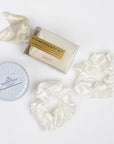 BOXFOX Gift products including Pinch Provisions White Glitter Bridal Emergency Kit, Voluspa White Tin Candle and 2 Ivory Silk Scrunchies laid out on white background