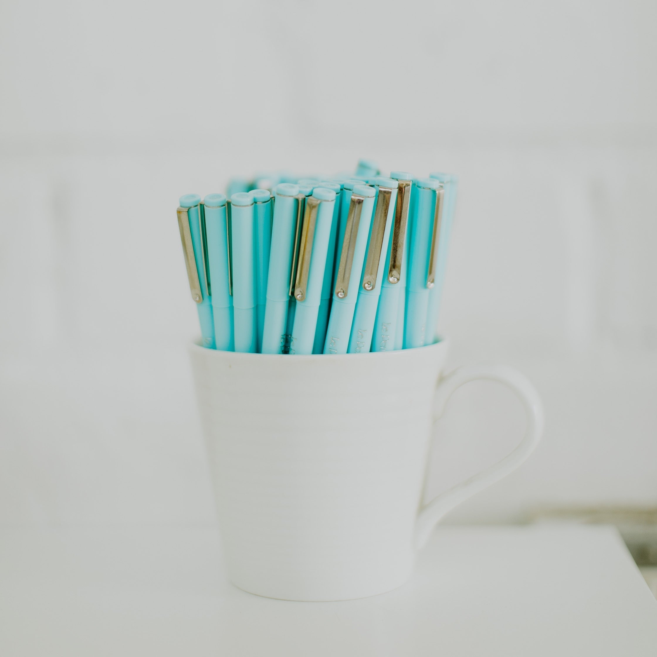 White mug with handful of pale blue pens filling it.