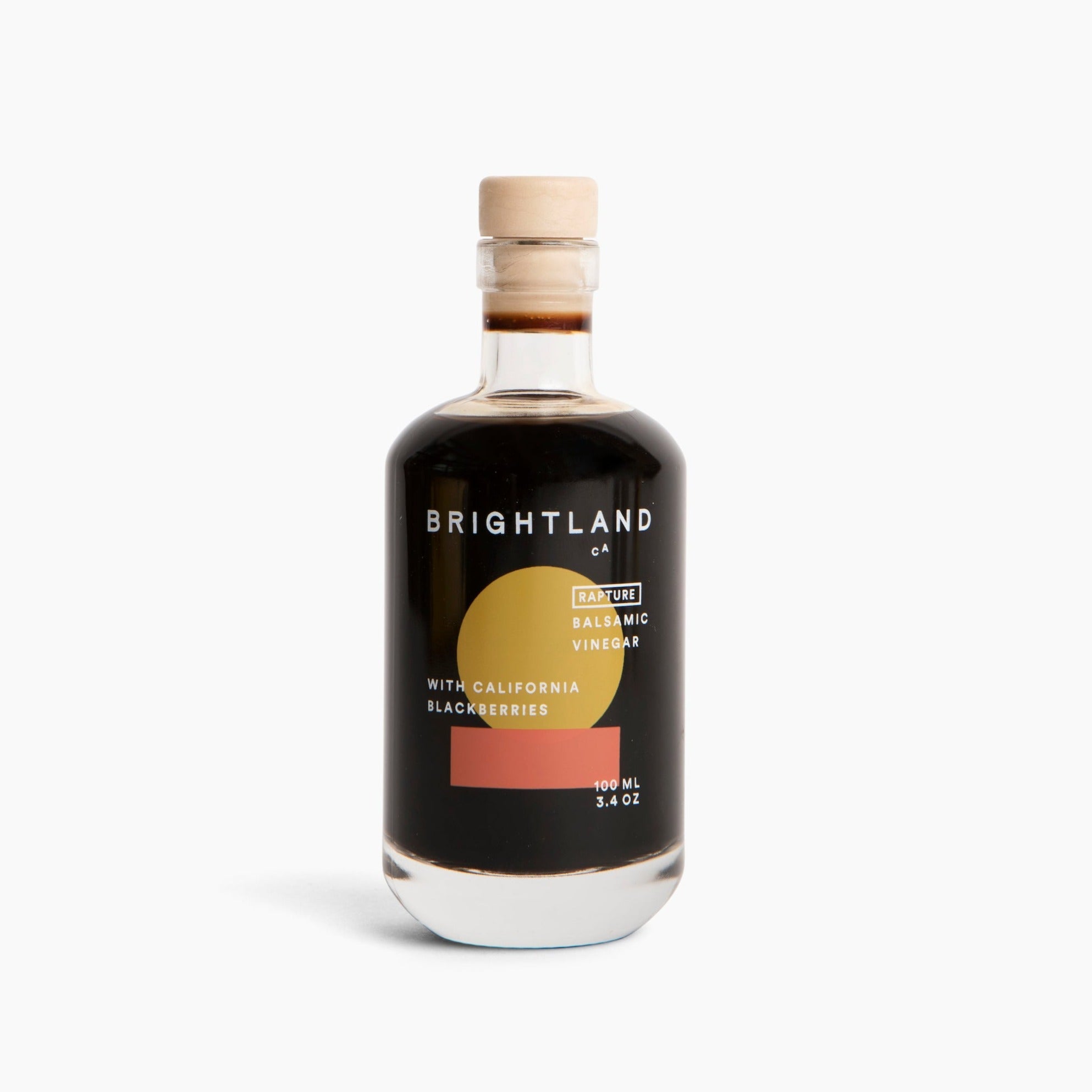 A glass bottle with beige cork topper containing dark brown vinegar. White Text on bottle reads, &quot;Brightland CA Rapture Balsamic Vinegar With California Blackberries 200mL 3.4 oz&quot;. Photographed on white background. 