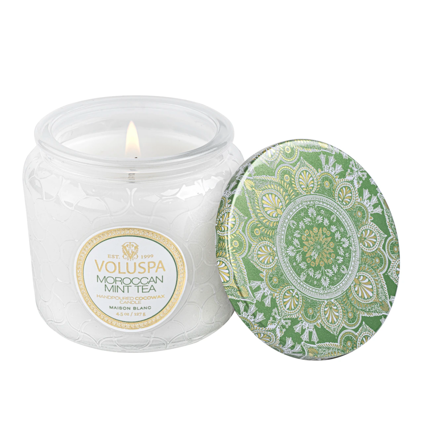 Small white candle with green and gold patterned lid tilted against the candle.