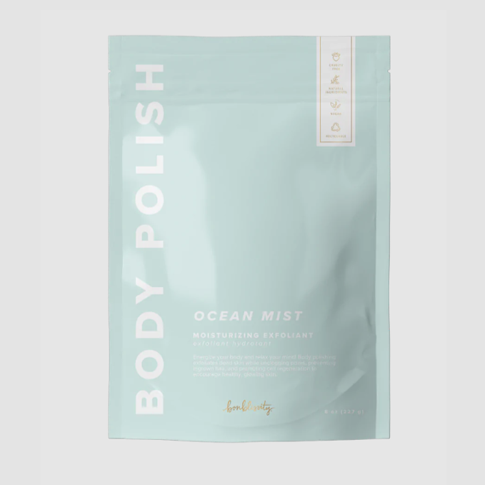 Rectangular, sealed, light blue plastic bag with white text that reads &quot;BODY POLISH&quot; on the side and &quot;OCEAN MIST MOISTURIZING EXFOLIANT&quot; in bottom right. Photographed on grey background. 
