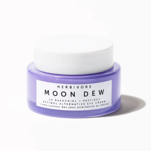 A stout purple glass container with white plastic lid. White label on jar reads, &quot; Herbivore Moon Dew 1% Bakuchiol + Peptides Retinol Alternative Eye Cream&quot; in black text. Photographed on white background. 