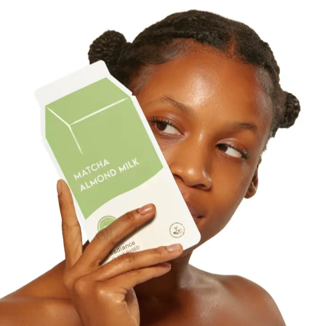 Young black woman holding up ESW Matcha Almond Milk Radiance Plant-Based Milk Sheet Mask in front of face