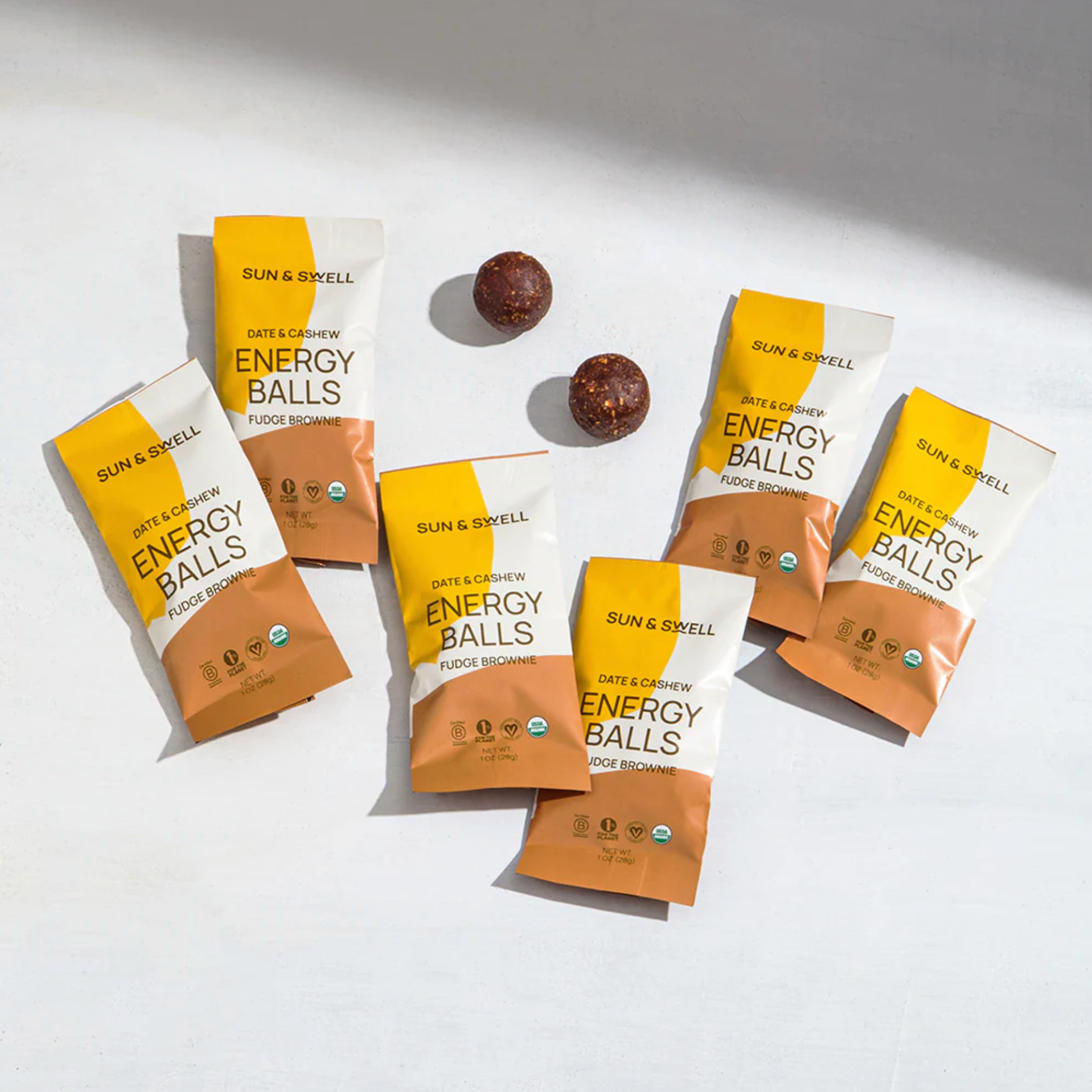 Set of the Sun &amp; Swell Date &amp; Cashew Energy Balls in fudge brownie. Packaging is a white background with yellow and brown circular design.