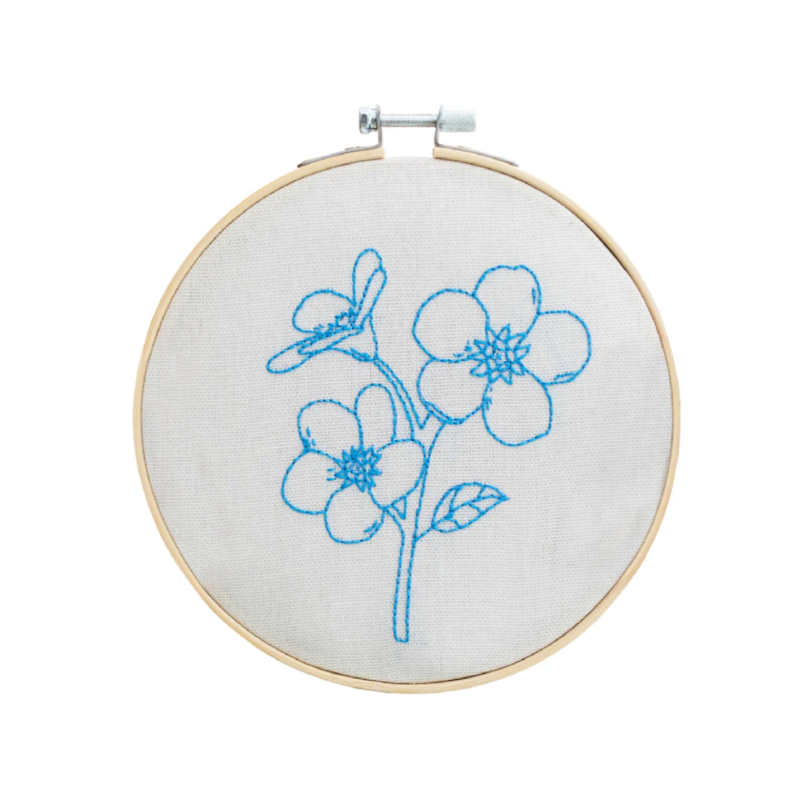 Embroidery hoop of a white piece of fabric and blue string that&#39;s stitch pattern is in the shape of forget me not flowers.