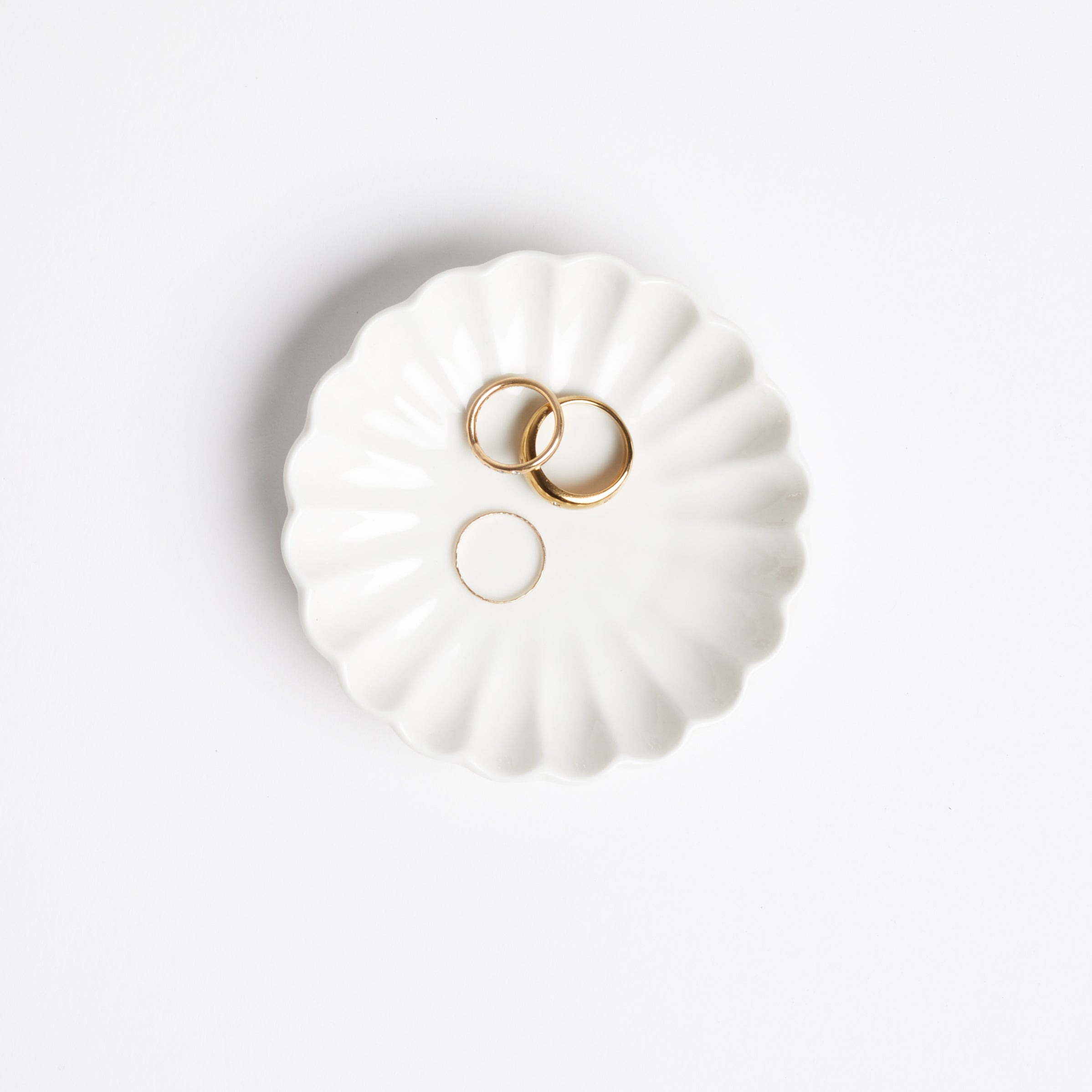 White scallop ring dish with gold rings on white background