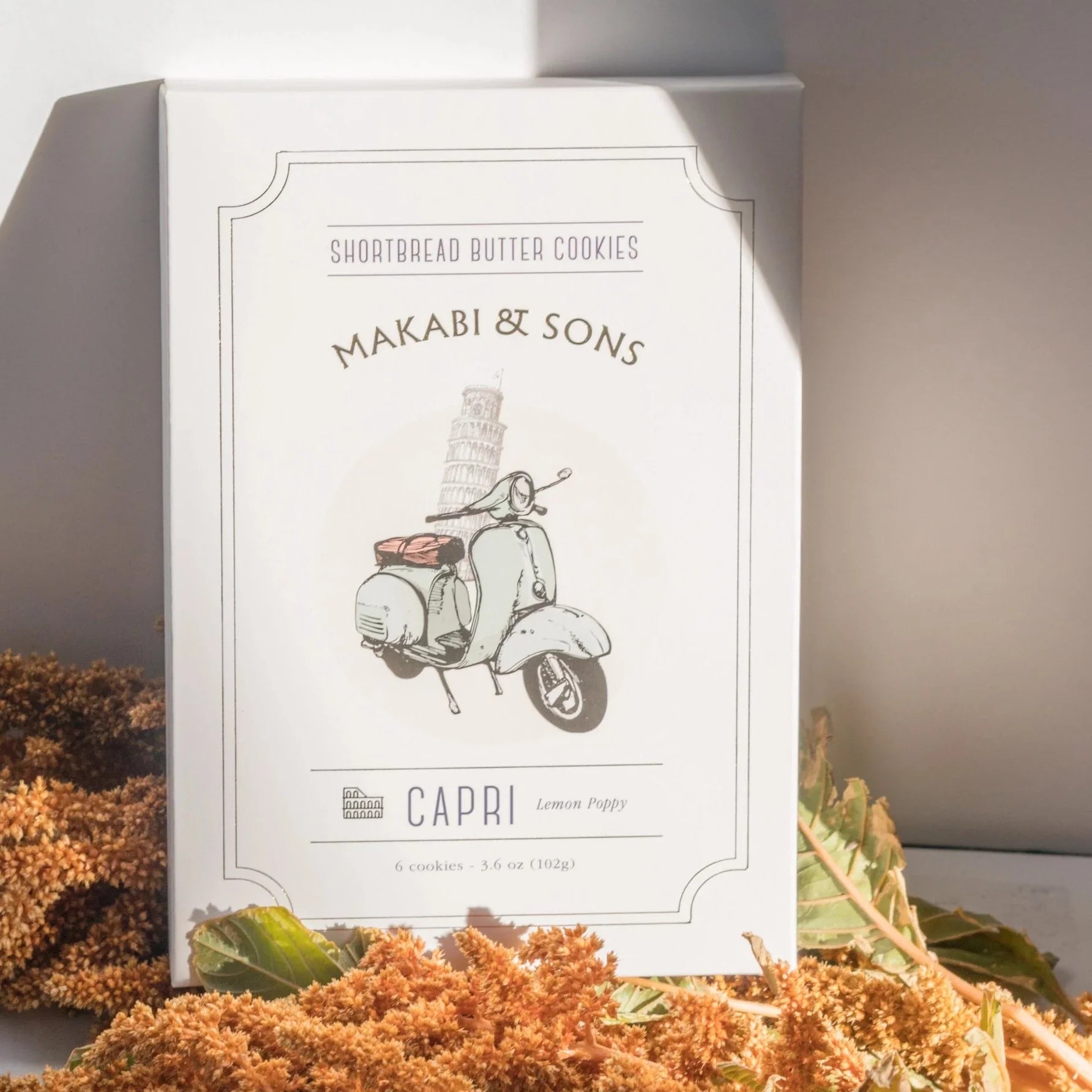 Box of shortbread cookies with vespa in front of leaning tower of pisa graphic with flowers laying in front of it