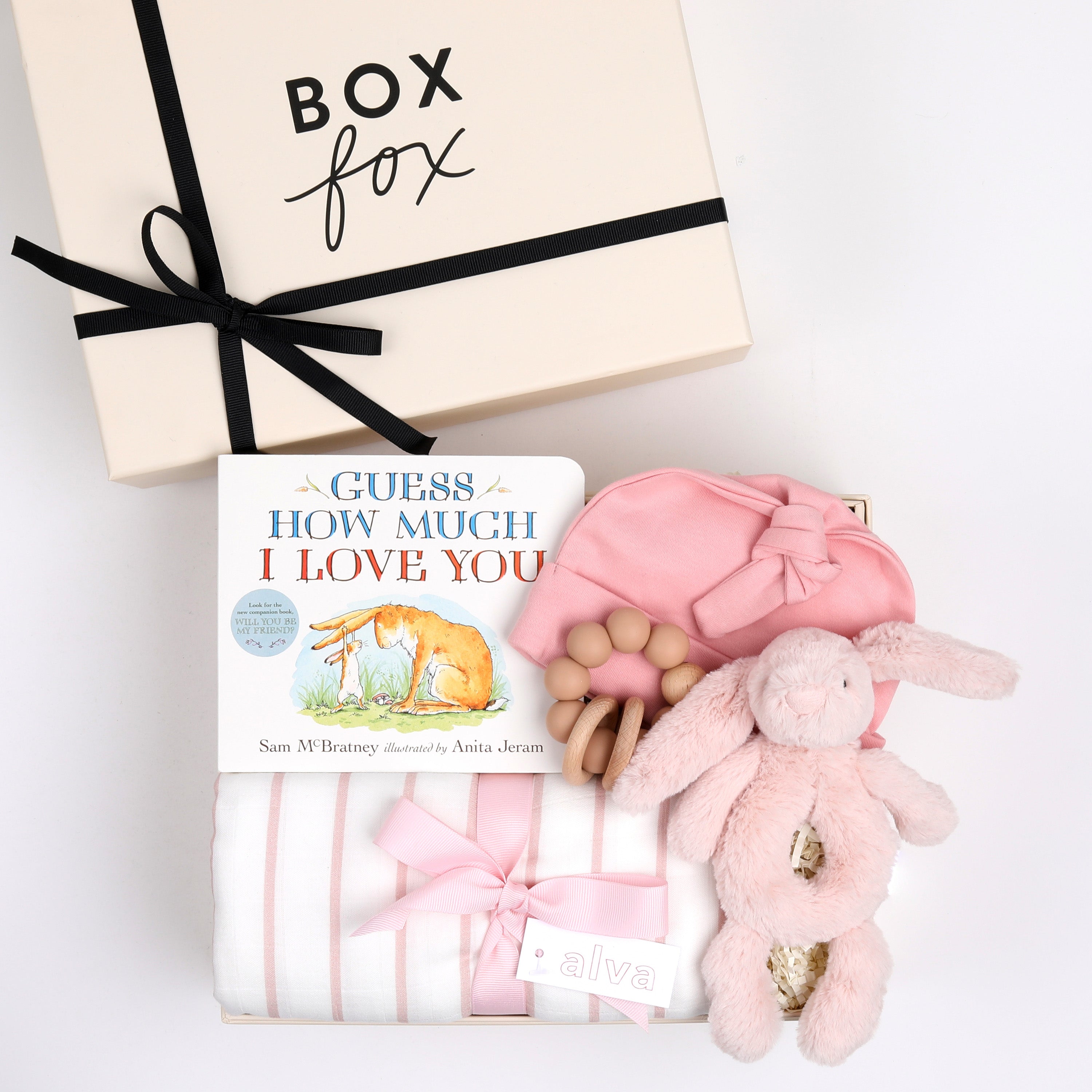 BOXFOX creme gift box next to open box containing a book, swaddle, teether, baby beanie and bunny rattle.