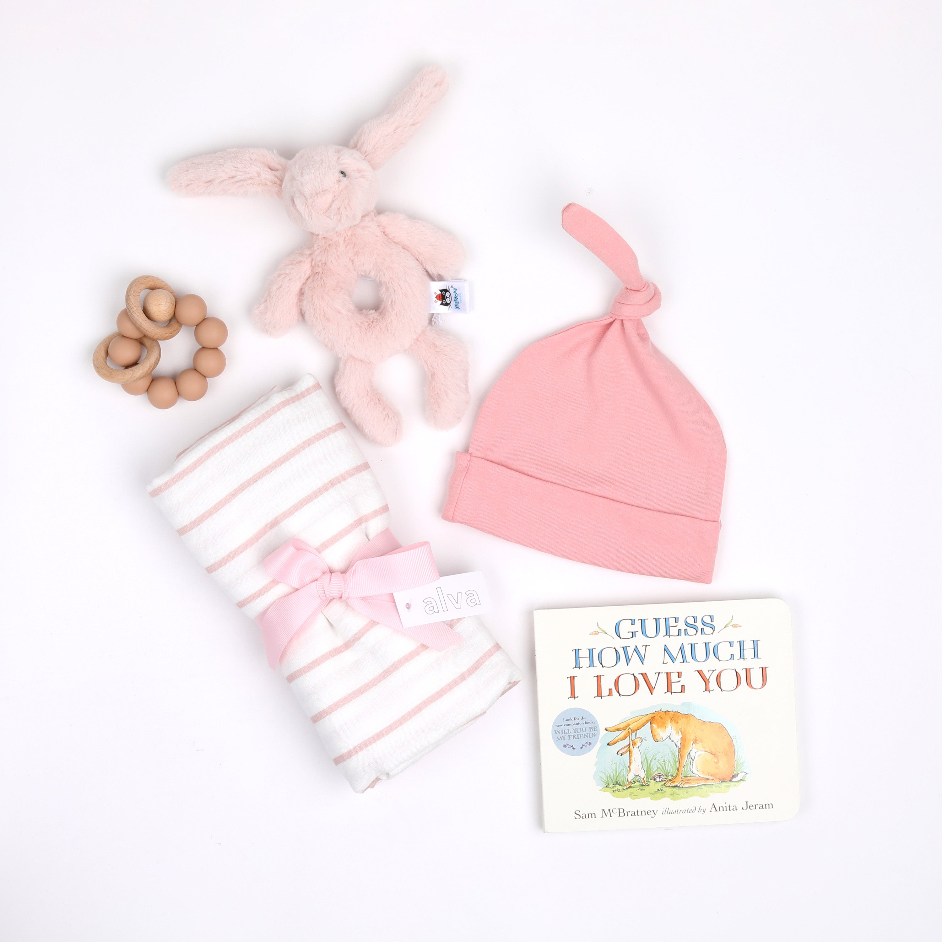 New Baby Girl products in a pile: teether, rattle, swaddle, hat, and book