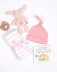 New Baby Girl products in a pile: teether, rattle, swaddle, hat, and book