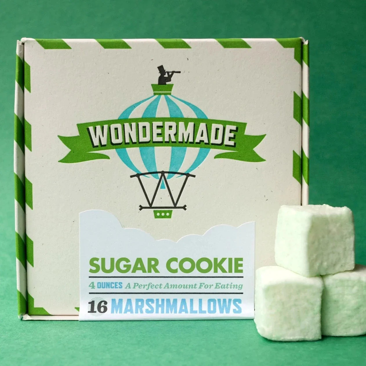 Cream square box with green lines. Box has company name and marshmallow flavor printed on the front. Three marshmallows next to the box.