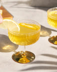 Gatsby Coupe Glasses filled with yellow liquid and lemon wedges